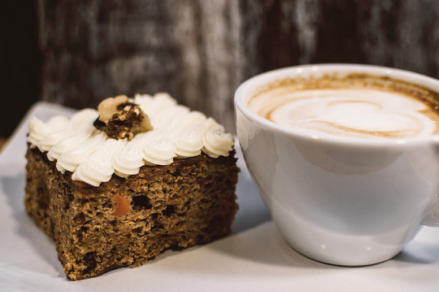 A slice of coffee and walnut cake next to a cup of hot coffee.